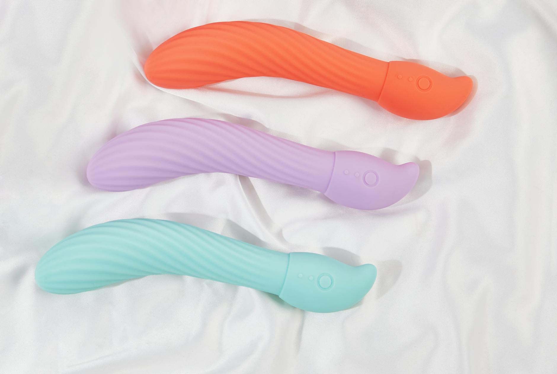 Trois vibromasseurs colorés disposés sur du tissu blanc, mettant en évidence leur texture lisse