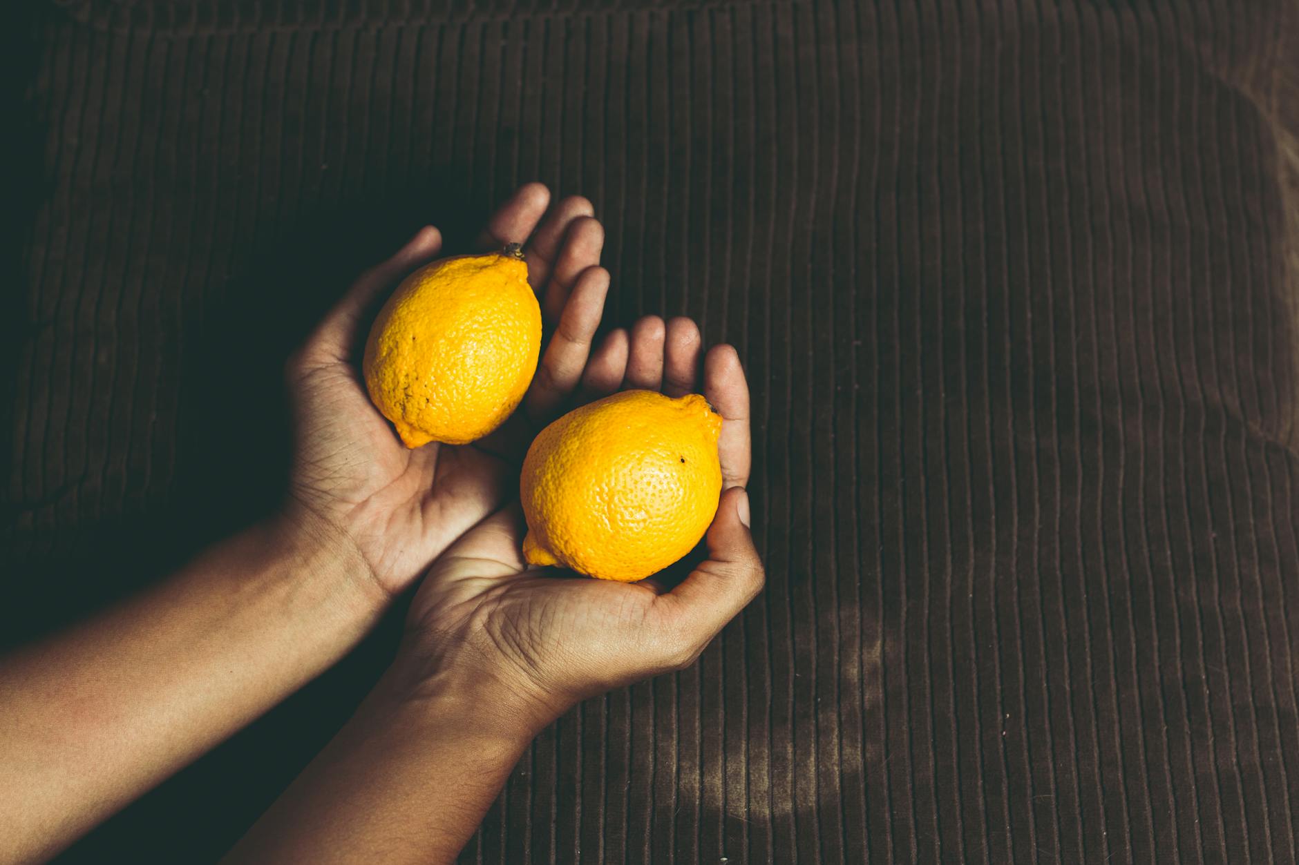 Deux mains tenant des citrons frais sur une surface marron, symbolisant la fraîcheur et le renouveau