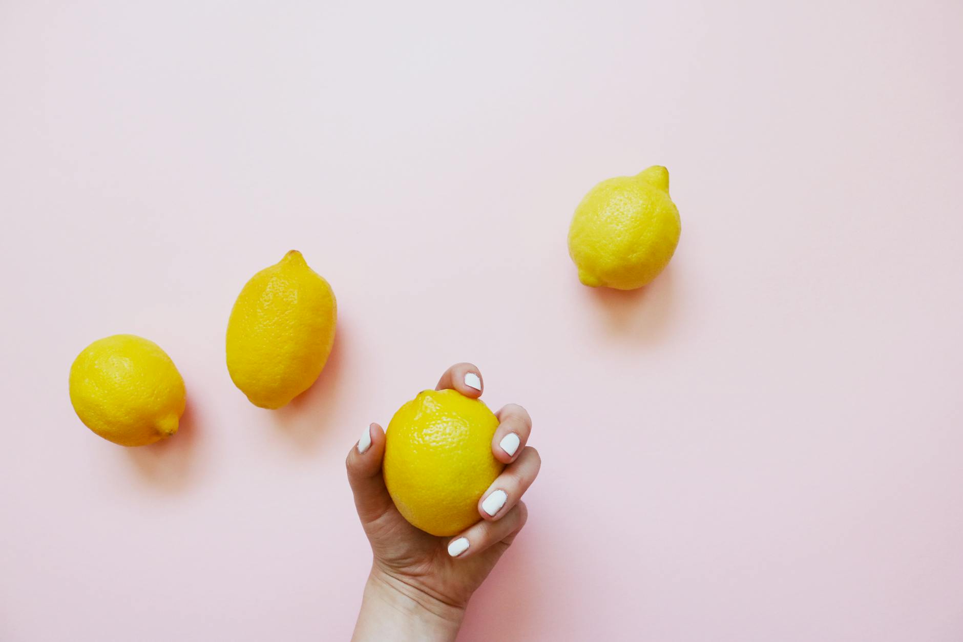Une main tenant un citron frais sur un fond rose pastel, symbole de plaisir naturel et sain