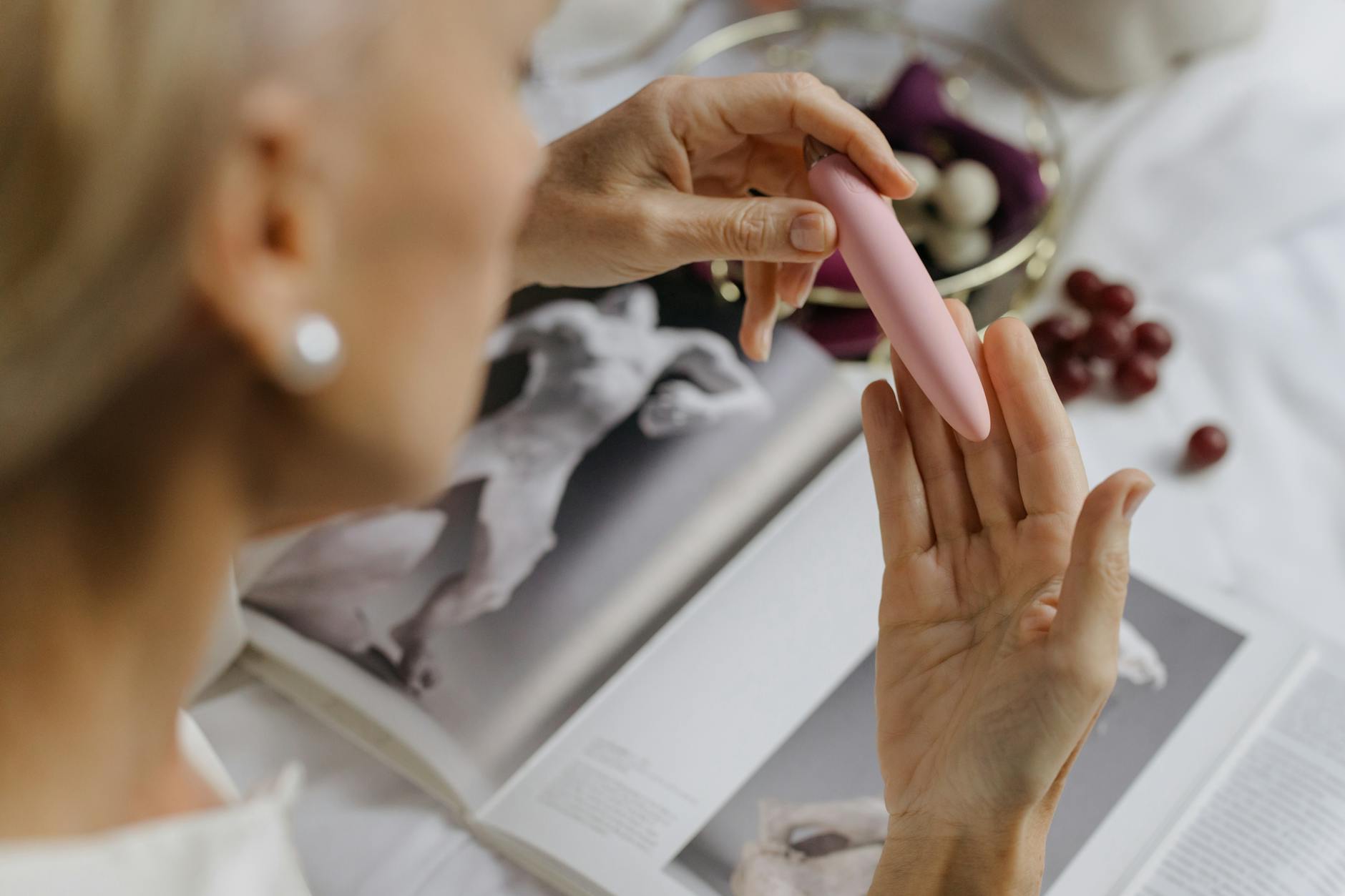Close-up of someone holding a pink vibrator with art books in the background, symbolizing intimate reconnection