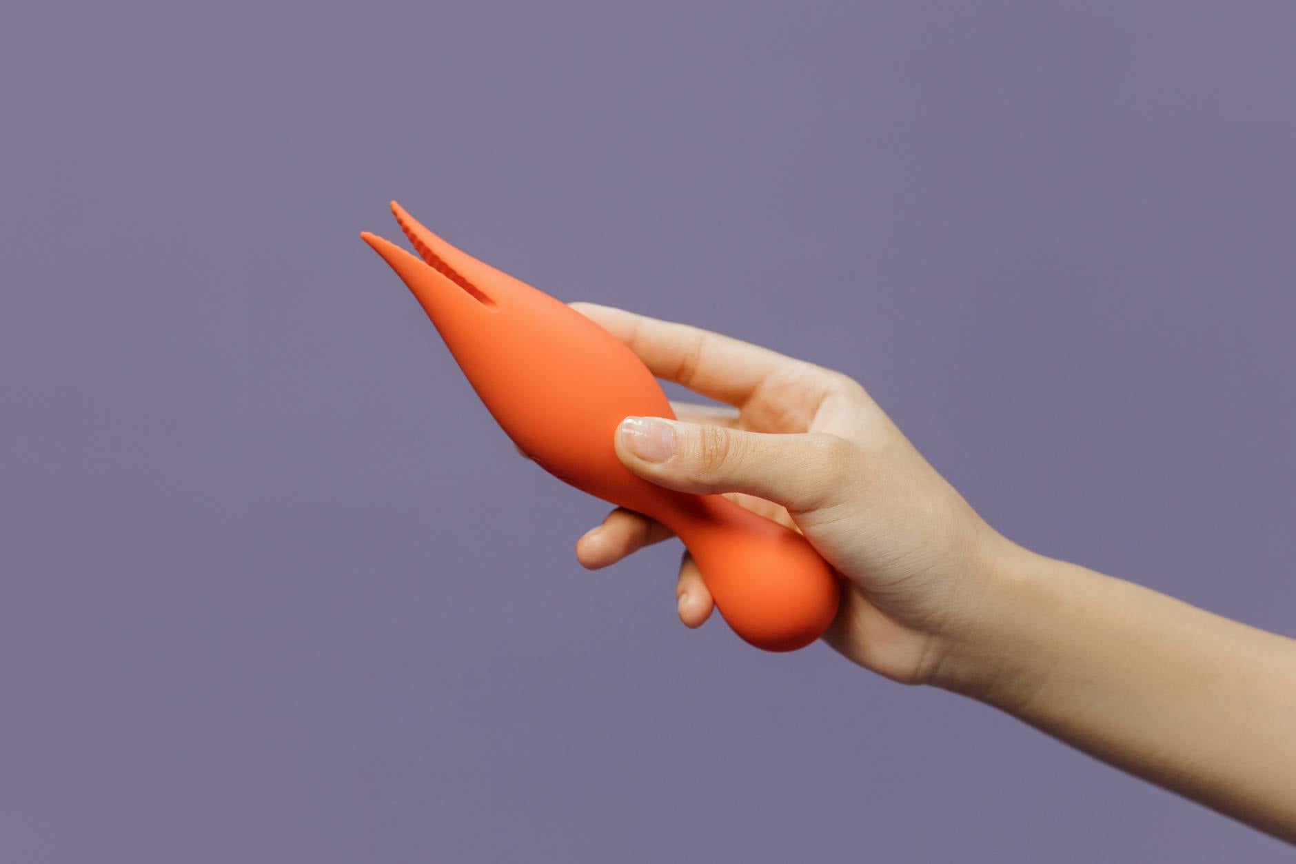 Vue rapprochée d'une main tenant un vibromasseur citron contre un fond violet minimaliste, mettant en avant la sensualité moderne.