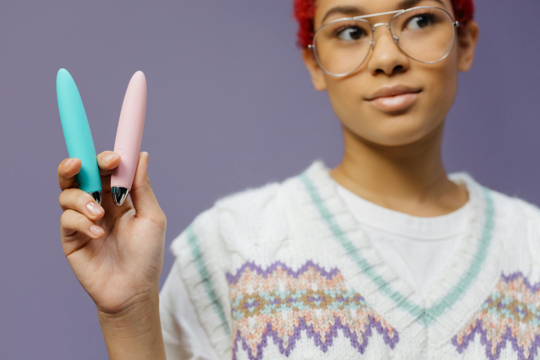 Une jeune femme tient deux vibromasseurs colorés contre un fond violet