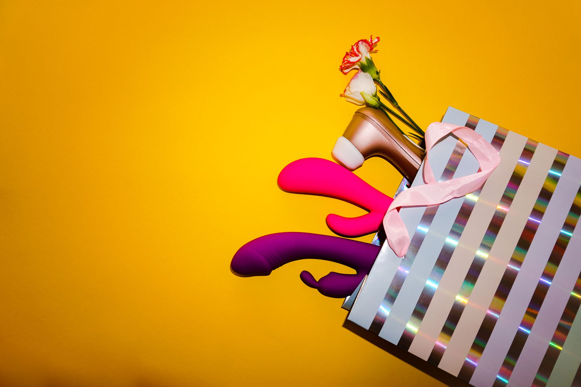 Vibromasseurs colorés avec des fleurs dans un sac cadeau holographique sur fond jaune vif